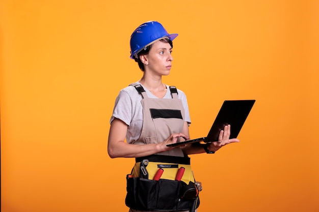 Konzentrierter Bauarbeiter hält drahtlosen PC vor der Kamera und nutzt Laptop, um im Studio Baumaterialien oder Inspiration zu finden. Bauarbeiterin liest Online-Website auf tragbarem Computer.