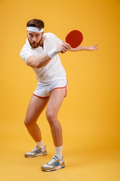 Konzentrierter emotionaler junger sportler, der schläger für tischtennis hält.