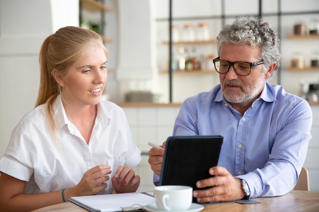 Konzentrierter freundlicher reifer männlicher Mentor, der dem Praktikanten die Arbeitsdetails erklärt