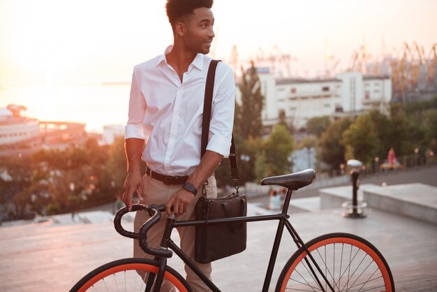 Konzentrierter junger afrikanischer Mann am frühen Morgen mit Fahrrad