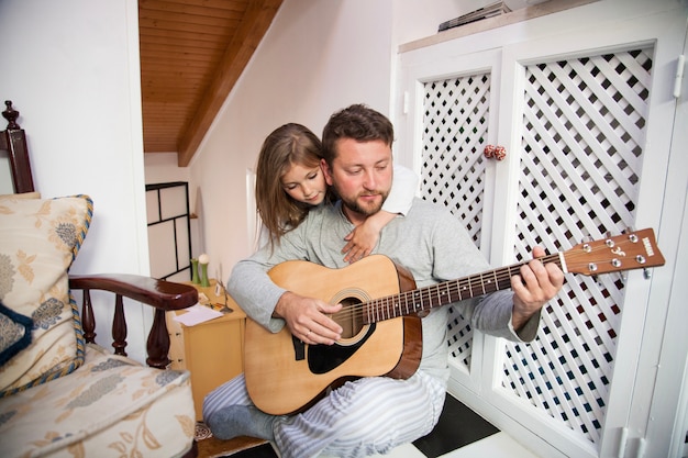 Konzentrierter Vater spielt Gitarre mit seiner Tochter und sieht ihn an