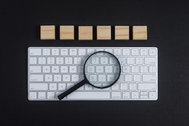 Konzept der Forschung mit Tastatur, Lupe, Holzwürfeln auf schwarzem Schreibtischhintergrund flach liegen. horizontales Bild