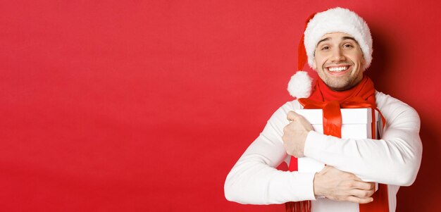 Konzept der Winterferien Weihnachten und Lifestyle-Bild des schönen Kerls in Weihnachtsmütze und Schal huggin