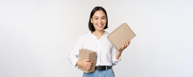 Konzept des Einkaufs und der Lieferung Junge glückliche asiatische Frau, die mit Kästen aufwirft und über weißem Hintergrund lächelt