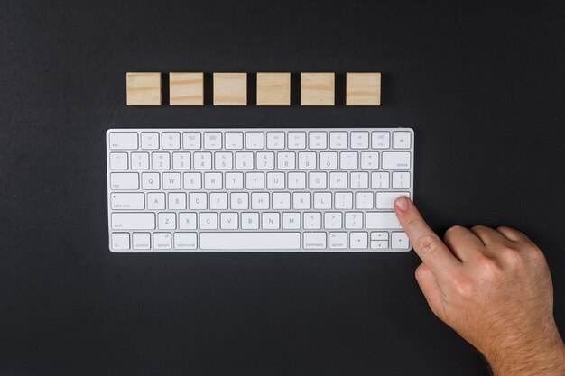 Konzept des Forschungsmannes, der die Eingabetaste drückt. mit Tastatur, Holzwürfel auf schwarzem Schreibtischhintergrund flach liegen. horizontales Bild