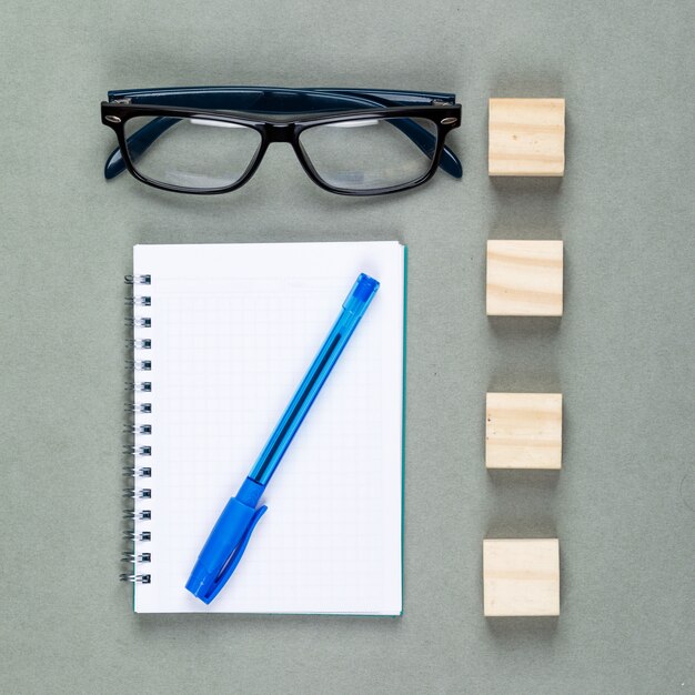 Konzept des Notierens mit Notizbuch, Stift, Brille, Holzelementen auf grauer Hintergrundoberansicht.