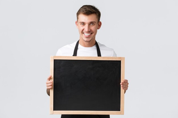 Konzept für kleine Einzelhandelsunternehmen, Café- und Restaurantmitarbeiter. Freundlicher gutaussehender Verkäufer kündigt den Kunden etwas an, hält eine Tafel ohne Schilder, lächelt glücklich, weißer Hintergrund