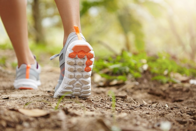 Konzept für Sport, Fitness, Natur und gesunden Lebensstil. Junger weiblicher Läufer, der Turnschuhe oder Laufschuhe beim Wandern oder Joggen im Park am sonnigen Tag trägt.