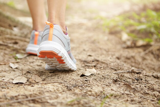 Konzept für Sport, Fitness und gesunden Lebensstil. Einfrieren der Aktion in der Nähe des weiblichen Läufers, der auf Fußweg geht oder joggt. Junge athletische Frau, die Laufschuhe beim Wandern im Park trägt.