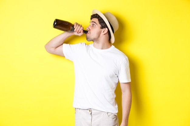 Konzept von Tourismus und Urlaub. Mann trinkt Wein aus der Flasche an Feiertagen, stehend vor gelbem Hintergrund. Platz kopieren