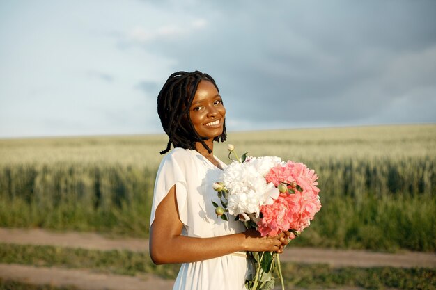 Konzept zum Internationalen Frauentag. Glückliche junge Frau des Afroamerikaners mit Bündel Pfingstrosenblumen.