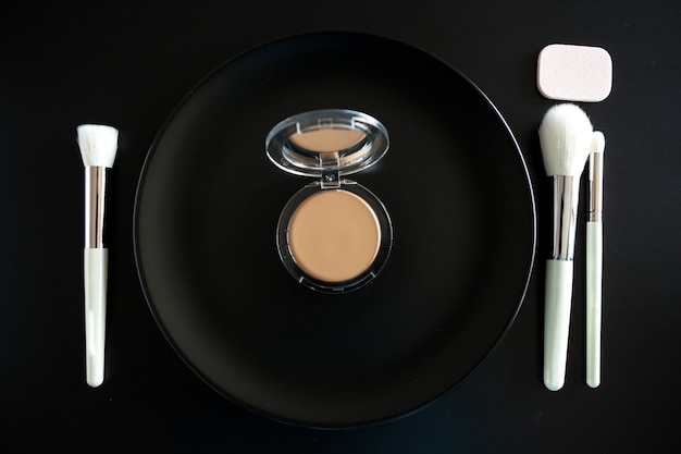 Konzeptionelles Bild von Make-up-Pinseln neben dem Teller auf schwarzem Hintergrund