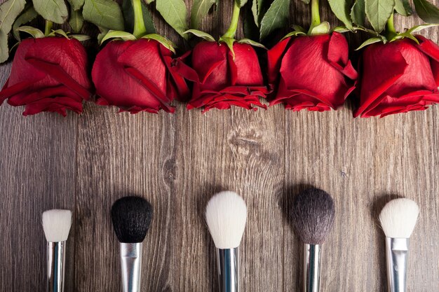 Konzeptionelles Bild von Make-up-Pinseln neben Rosen auf Holzuntergrund