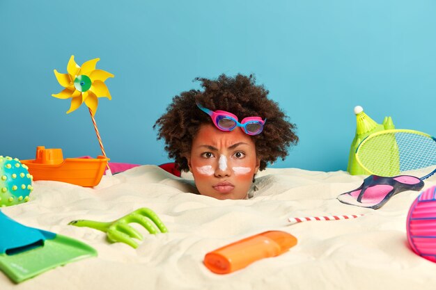 Kopf der jungen Frau mit Sonnenschutzcreme auf Gesicht umgeben von Strandaccessoires