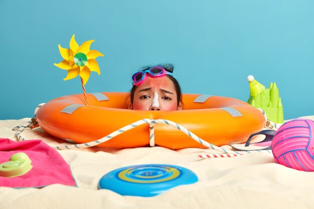 Kopf der jungen Frau mit Sonnenschutzcreme auf Gesicht umgeben von Strandaccessoires