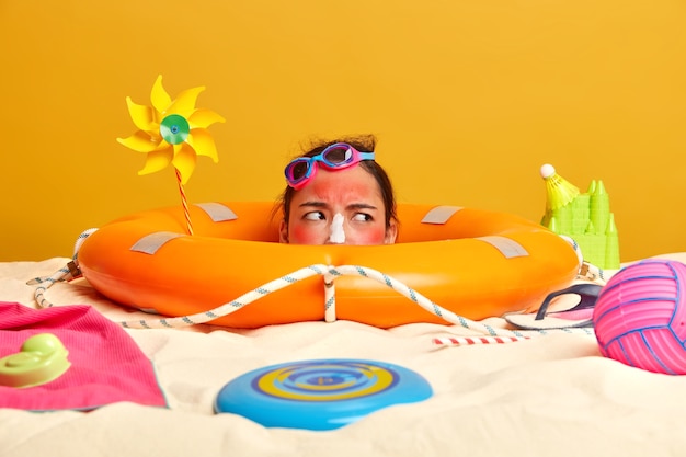 Kopf der jungen Frau mit Sonnenschutzcreme auf Gesicht umgeben von Strandaccessoires