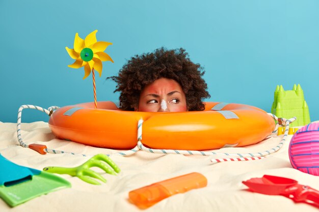 Kopf der jungen Frau mit Sonnenschutzcreme auf Gesicht umgeben von Strandaccessoires