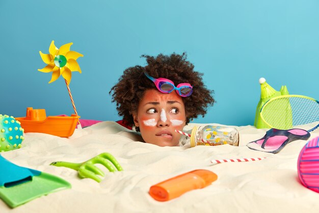 Kopf der jungen Frau mit Sonnenschutzcreme auf Gesicht umgeben von Strandaccessoires