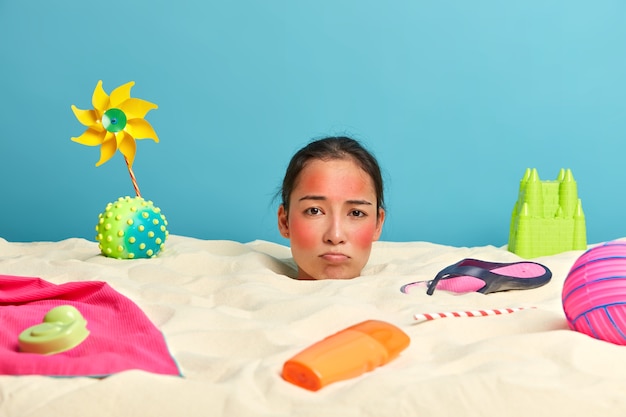 Kopf der jungen Frau mit Sonnenschutzcreme auf Gesicht umgeben von Strandaccessoires