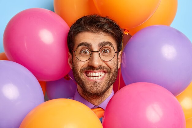 Kopfschuss des gutaussehenden Kerls, umgeben von Partyballons, die aufwerfen