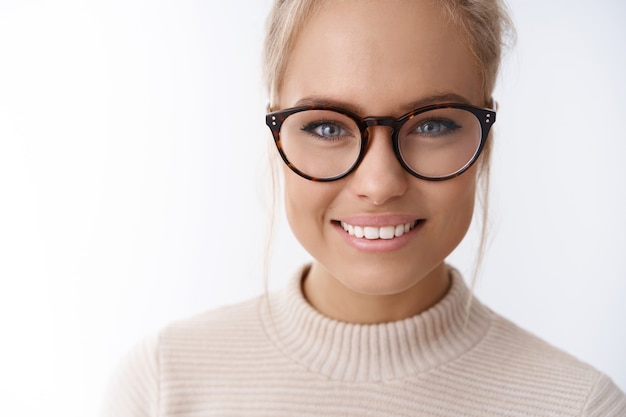 Kopfschuss einer hoffnungsvollen, verträumten, attraktiven, eleganten Frau in trendiger Brille mit gekämmtem Haar, die freundlich und amüsiert in die Kamera lächelt und Spaß daran hat, positive Emotionen vor weißem Hintergrund auszudrücken