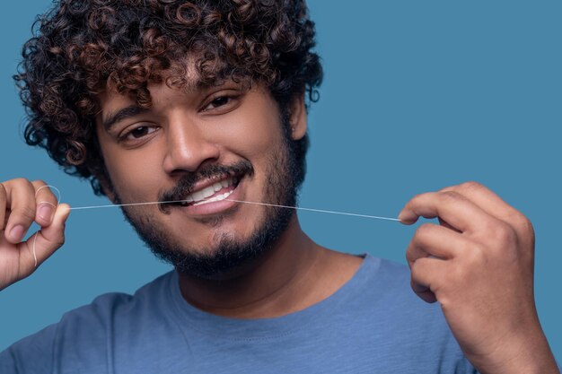 Kopfschuss eines gutaussehenden, erfreuten jungen Inders, der seine Zahnseide vor der Kamera benutzt