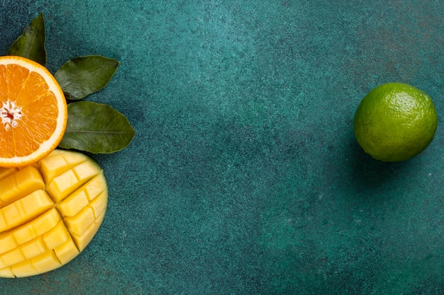 Kopierraum geschnitten geschnittene Mangos mit einer halben Orange und Bananen auf einem grünen Tisch