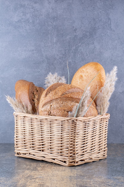 Kostenloses Foto korb gefüllt mit brotlaiben und federgrasstielen auf marmoroberfläche