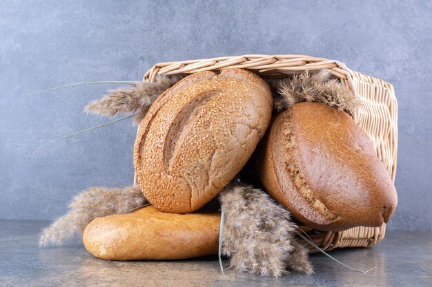 Korb gefüllt mit Brotlaiben und Federgrasstielen auf Marmoroberfläche