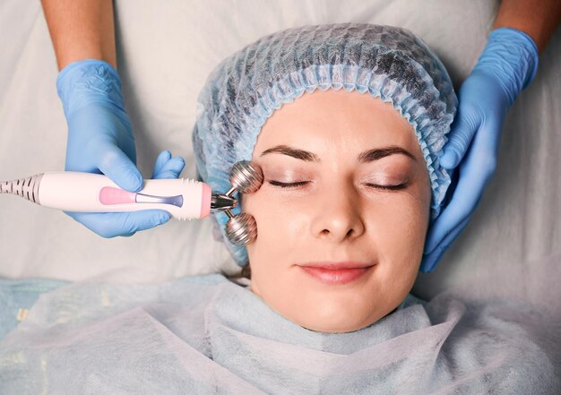 Kosmetikerin massiert Frauengesicht mit Gesichtsrolle