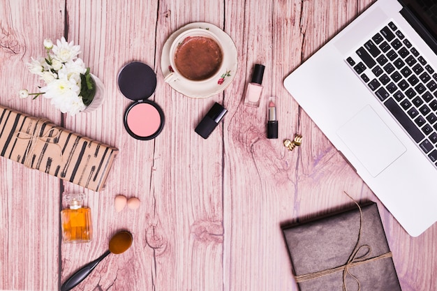 Kosmetische Produkte; Vase; Tagebuch und Laptop auf rosa hölzernem strukturiertem Hintergrund