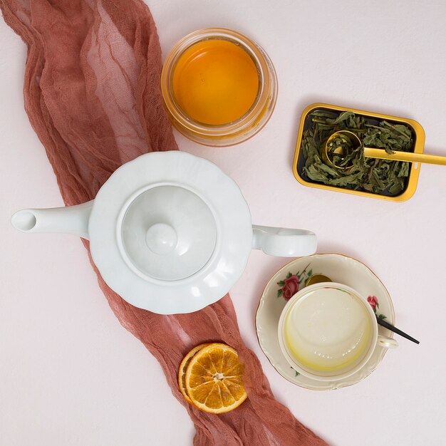 Kräuter; getrocknete Zitronenscheiben; Teekanne; Honigglas mit braunem Textilstoff über dem konkreten Hintergrund
