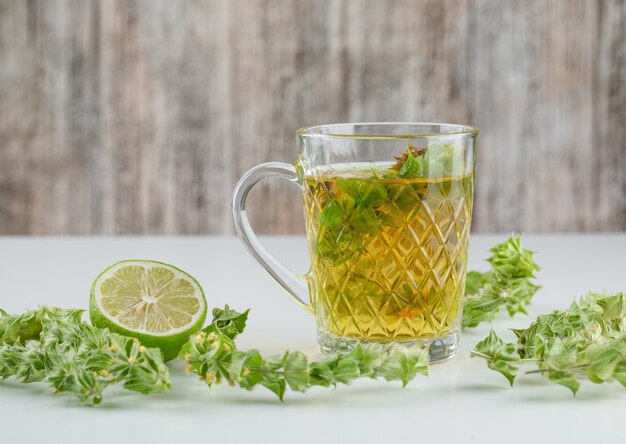 Kräutertee in einer Glasschale mit Blättern, Limettenseitenansicht auf Weiß und grungy