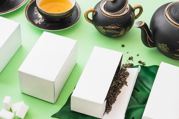 Kräutertee-Kisten mit Tee und Zuckerwürfeln auf grünem Hintergrund