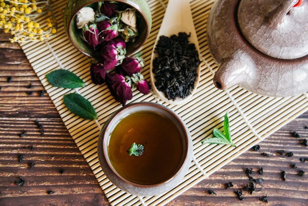 Kräuterteetasse mit getrockneter rosafarbener Blume und trockenen Blättern auf Tischset