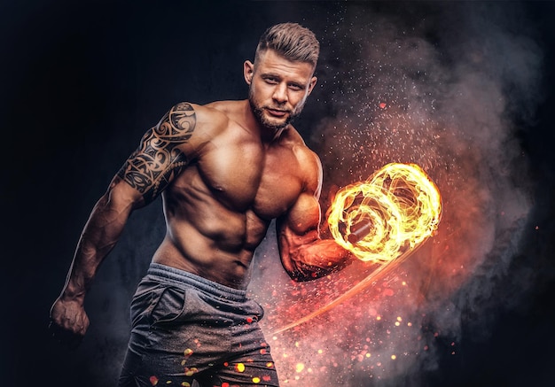 Kraftvoller, stylischer Bodybuilder mit Tätowierung auf dem Arm, der die Übungen auf einem Bizeps mit Hanteln macht, schaut mit einem selbstbewussten Blick auf die Kamera. Konzept der Feuerkunst.