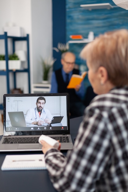 Kranke ältere Frau im Gespräch mit jungem Arzt während der Fernsprechstunde talking