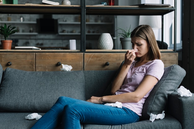 Kranke Frau, die auf dem Sofa sitzt, das ihre Nase durchbrennt