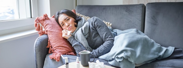 Kostenloses Foto kranke frau, die zu hause auf dem sofa liegt und sich ein erkältetes junges mädchen einfängt, das aufgrund von heizungsproblemen in ihr friert