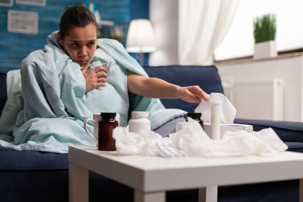 Kranke Frau in Decke sitzt zu Hause mit Coronavirus