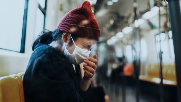 Kranke Frau in einer Maske, die während der Coronavirus-Pandemie in einen Zug niest