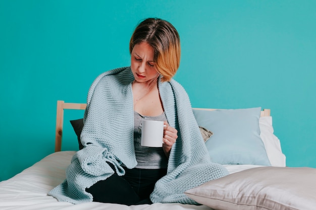 Kranke Frau mit Tasse auf dem Bett