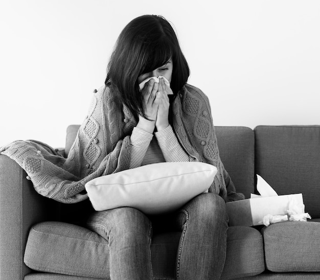 Kranke Frau niesen auf dem Sofa Graustufen