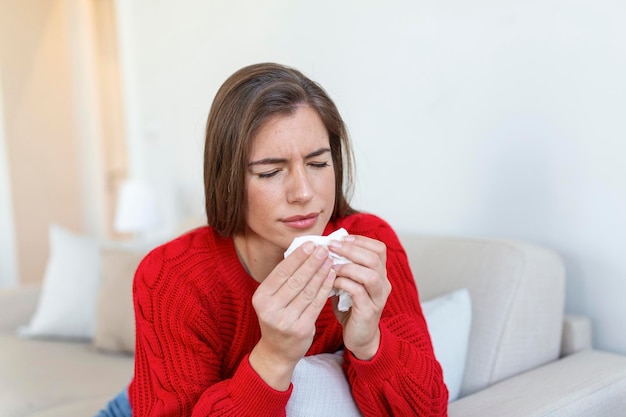 Kranke Frau sitzt auf dem Bett und fühlt sich ungesund. Schnupfen läuft. Kranke junge Frau, die an Rhinitis leidet, Schnupfen mit Atemwegsinfektion, bekommt Grippe, braucht Medikamente