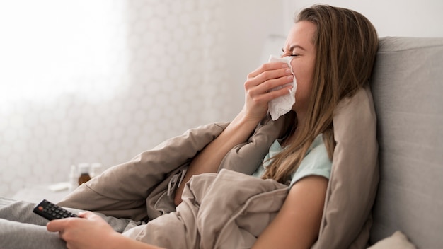 Kranke Frau sitzt im Bett und putzt sich die Nase