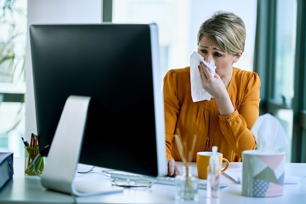 Kostenloses Foto kranke geschäftsfrau, die nase weht, während sie an einem computer im büro arbeitet