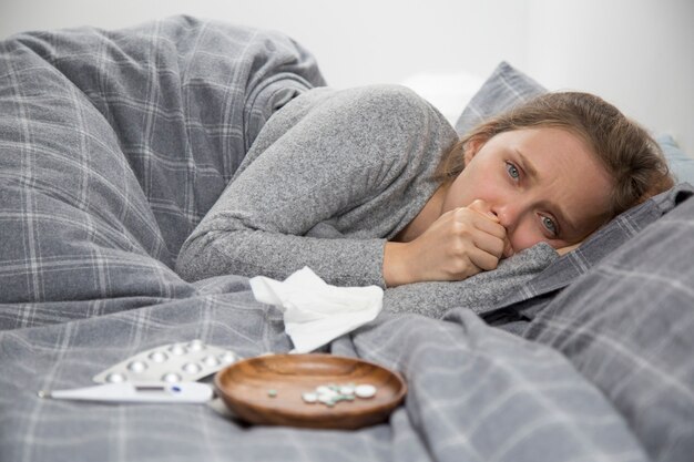 Kranke junge Frau, die im Bett liegt und husten