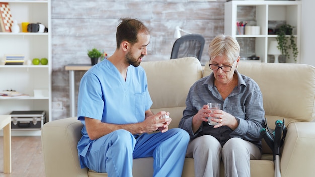 Krankenpfleger sitzt auf der Couch mit einer älteren Frau, die ihre medizinische Behandlung im Pflegeheim gibt.