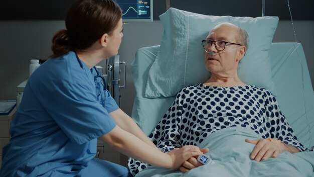 Krankenschwester aus der Krankenstation neigt zu kranken alten Patienten im Bett