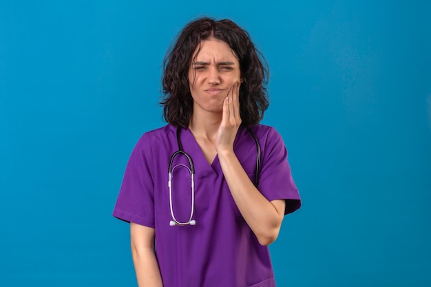Krankenschwester der jungen Frau in der medizinischen Uniform und mit dem Stethoskop, das Mund mit Hand mit schmerzhaftem Ausdruck wegen Zahnschmerzen berührt